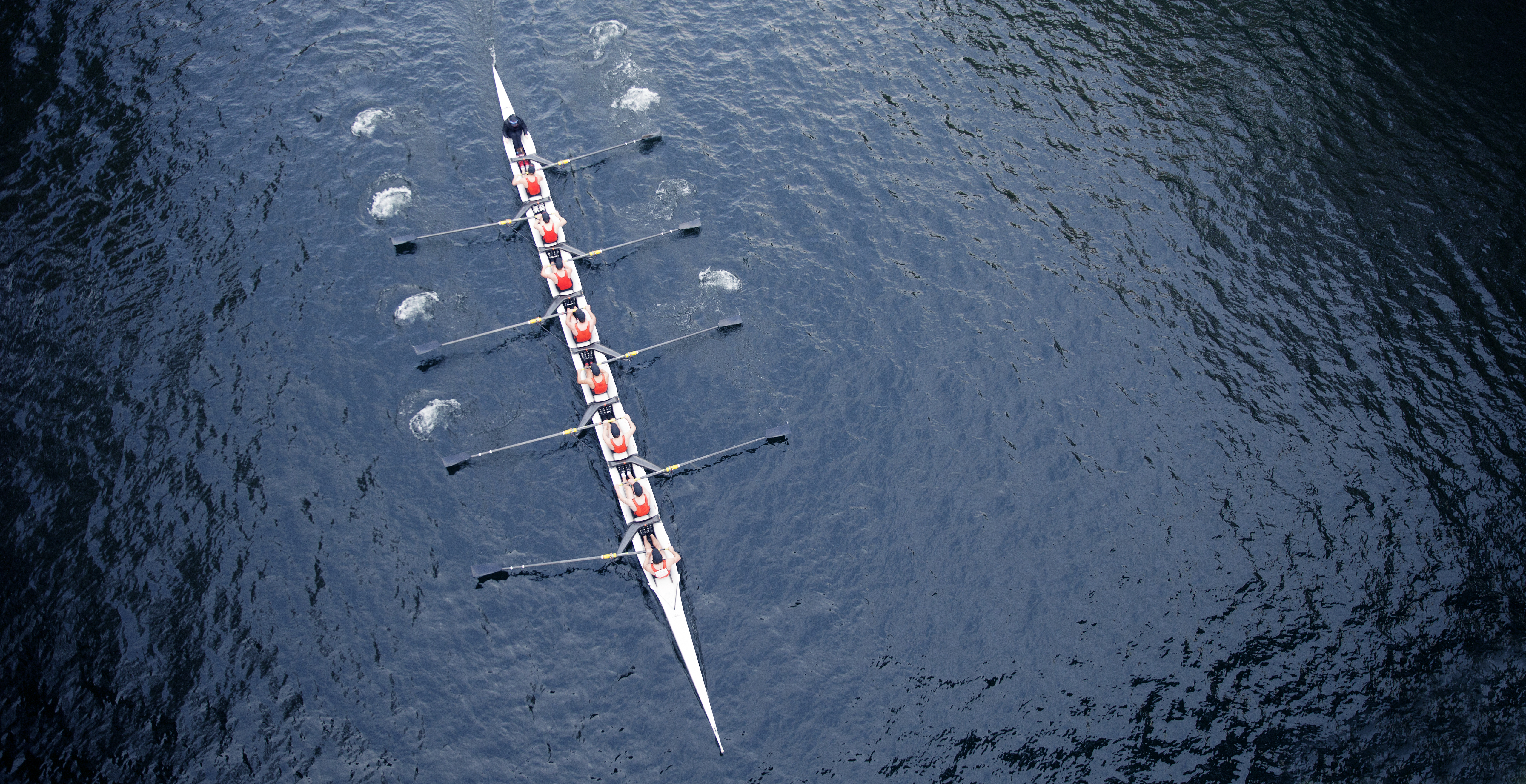 An eight-person rowing crew seen from above — consensus is eight oars in the water at the same moment